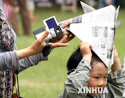 4月21日，一位母亲在帮助孩子戴上用旧报纸制成的太阳帽。 &nbsp;&nbsp;&nbsp;&nbsp;4月21日，来自英、美、日、韩等国的百余个家庭的家长和孩子齐聚上海动物园，在搭建的国际民族村，展开环境保护、生物多样性保护等活动，呼吁人们携手保护地球家园。4月22日是世界地球日。 新华社记者　张明摄　